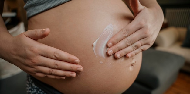 Close up pregnant female gently rubbing in cream on her belly