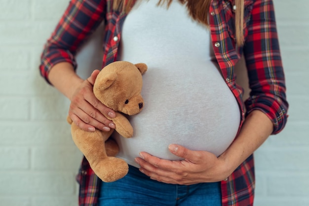 テディベアグッズで妊娠中の女性の腹のクローズアップ。