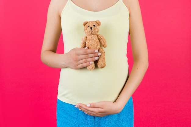 Close up of pregnant woman in colorful home clothing holding a teddy bear against her belly