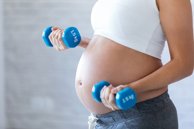 Close-up of pregnant woman doing exercise with dumbbells at home