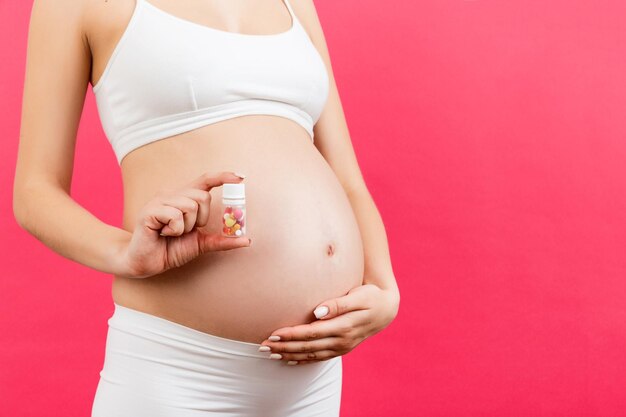 Close up of pregnant woman holding a bottle of pills against her belly at colorful background with copy space Taking medication during pregnancy concept