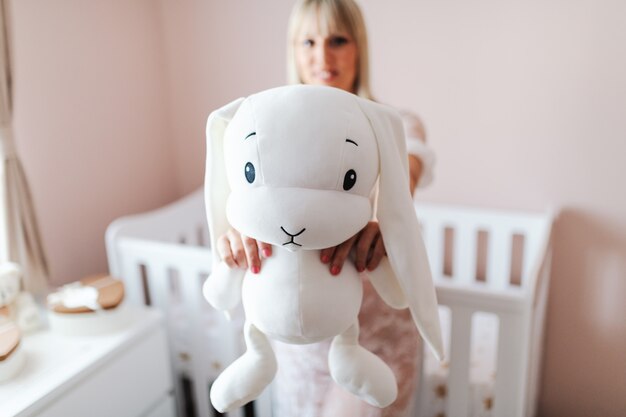 Close up of pregnant woman holding bunny toy while standing in baby room.