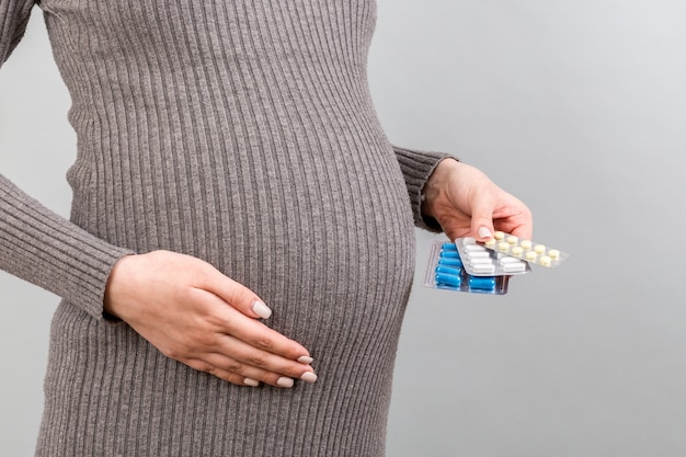 Close up of pregnant woman holding different blisters with pills