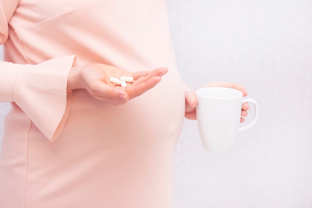 Close-up of pregnant woman holding a pill, vitamins. The concept of pregnancy, healthcare, gynecology, medicine and a healthy lifestyle. Mother is expecting a baby. Nutritional supplements.