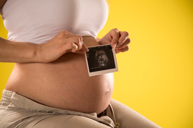 Chiuda in su della donna incinta che tiene la scansione ad ultrasuoni sulla sua pancia