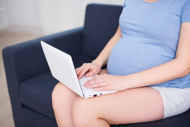 Close up of pregnant woman using laptop at home