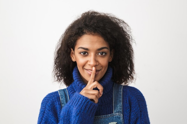 Close up of a pretty young african woman wearing sweater standing isolated, showing silence gesture