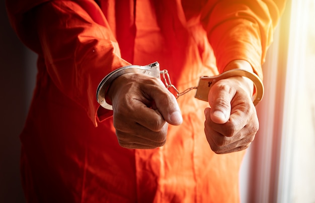 Photo close up of prisoner's hands with handcuffs in orange jumpsuit at prison