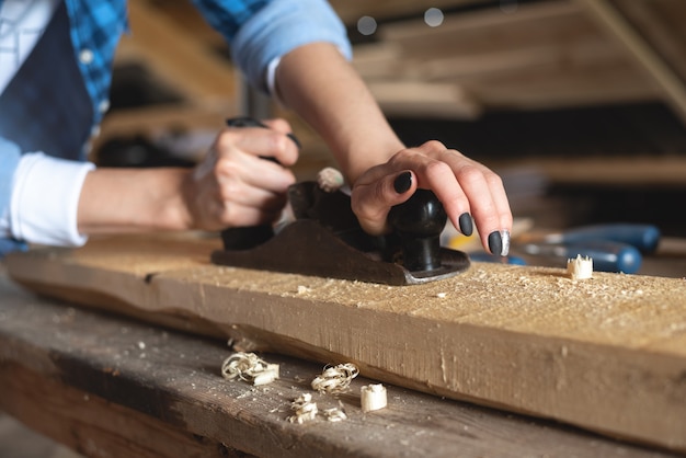 Close-up of the process of planing a wooden bar with a hand planer by women's hands