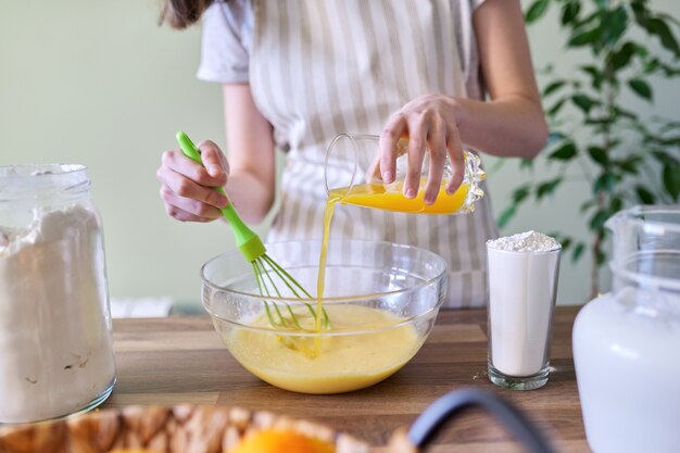 Close-up process of preparing orange pancakes, female hands pouring orange juice into a bowl with dough