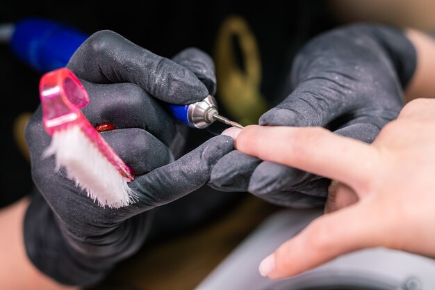 Close-up professional beautician hands working with electric drill on client fingernails. Procedure