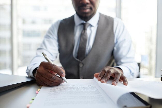 Крупный план профессионального черного бизнесмена, подписывающего документы за столом в офисе