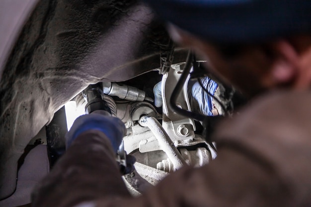 Close up Professional car mechanic makes repairs to the undercarriage of a supported car in auto repair service. Autoworker changes sleeves in garage of repair service station