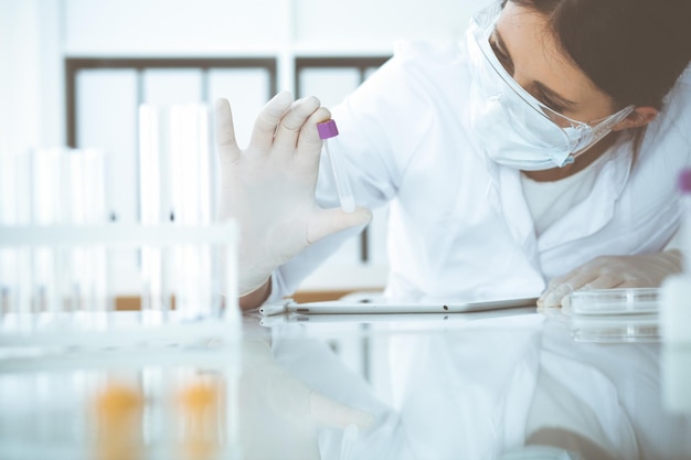 Primo piano di una scienziata professionista in occhiali protettivi che fa esperimenti con reagenti o analisi del sangue in laboratorio. medicina, biotecnologia e concetto di ricerca.