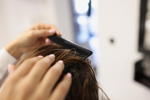 プロの美容師のクローズアップは、スタイリッシュなヘアカットを作成するための櫛を使用しています。ビューティーサロンで予約に座っているクライアントの女性。ファッション、理髪店のコンセプト