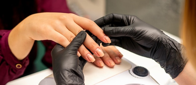 Close up professional manicure master holds the female hand of the customer and checks the manicure in a nail salon