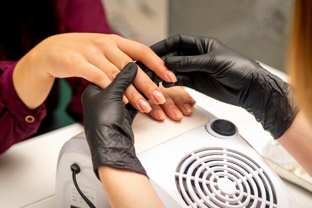 Close up professional manicure master holds the female hand of the customer and checks the manicure in a nail salon