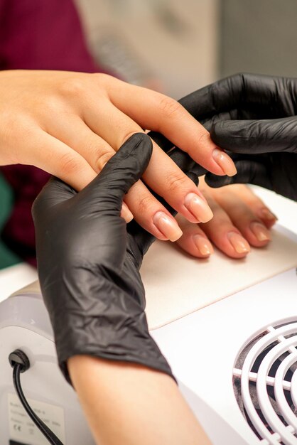 Close up professional manicure master holds the female hand of the customer and checks the manicure in a nail salon