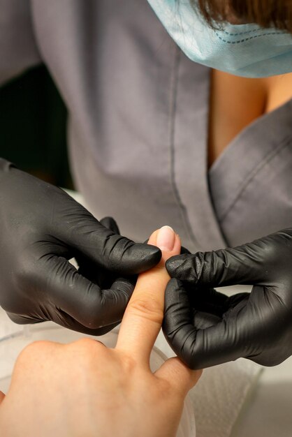 Close up professional manicure master holds the female hand of the customer and checks the manicure in a nail salon