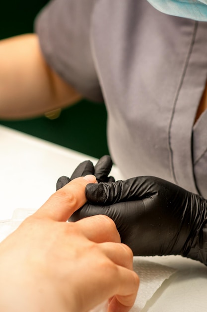 Close up professional manicure master holds the female hand of the customer and disinfects nails in a nail salon