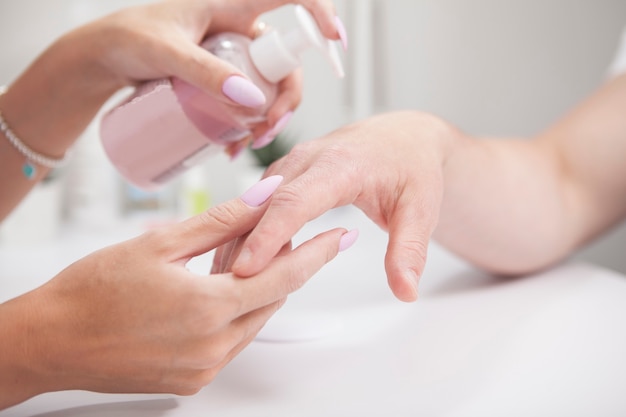 Close up of professional manicurist applying hand cream on male hands after manicure