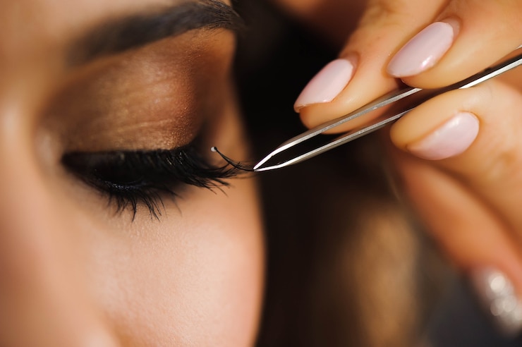 Photo close up of professional stylist lengthening lashes for female client in a beauty salon.