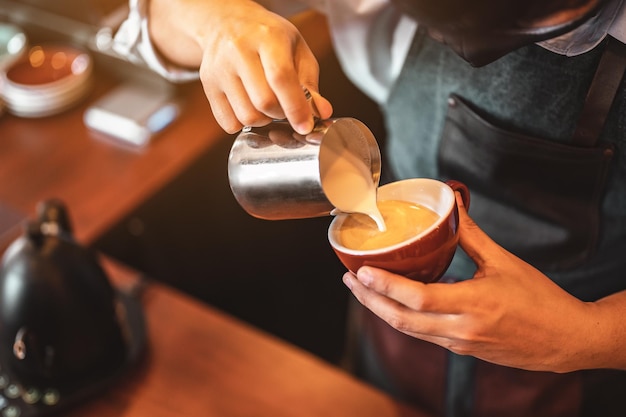 美しいラテアートを作るコーヒーカップに蒸し牛乳を注いでバリスタによって専門的にコーヒーを抽出するクローズアップ。コーヒー、抽出、ディープ、カップ、アート、バリスタのコンセプト。