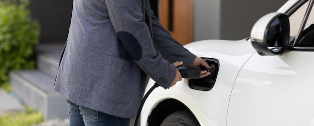 Close-up progressieve aziatische man laadt zijn EV-auto op bij het laadstation thuis