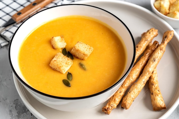 Photo close up of pumpkin carrot cream soup in a bowl with croutons pumpkin seeds and bread sticks