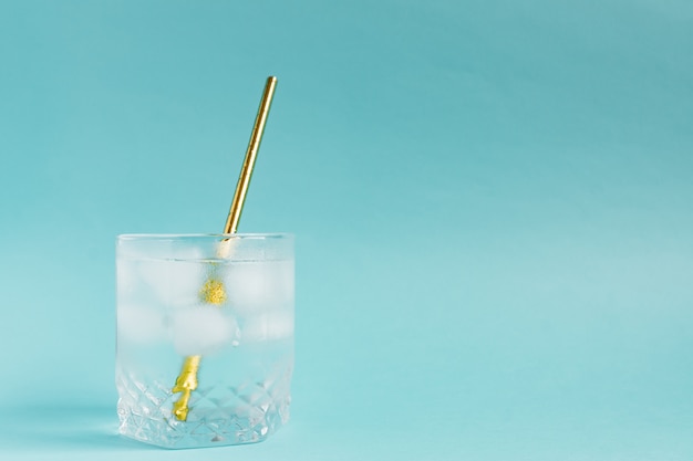 Close up of pure water with ice and paper straw in transparent glass and sun glare.