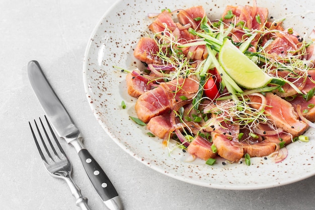 Close up of rare seared tuna slices with lime and arugula leaves on a plate.