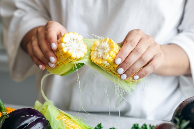 Close-up rauwe maïs in vrouwelijke handen in de keuken