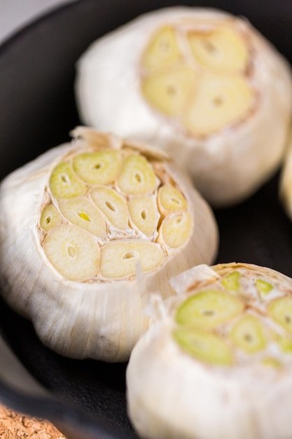 Foto primo piano di teste di aglio crudo in padella di ghisa per preparare la ricetta dell'aglio arrosto.