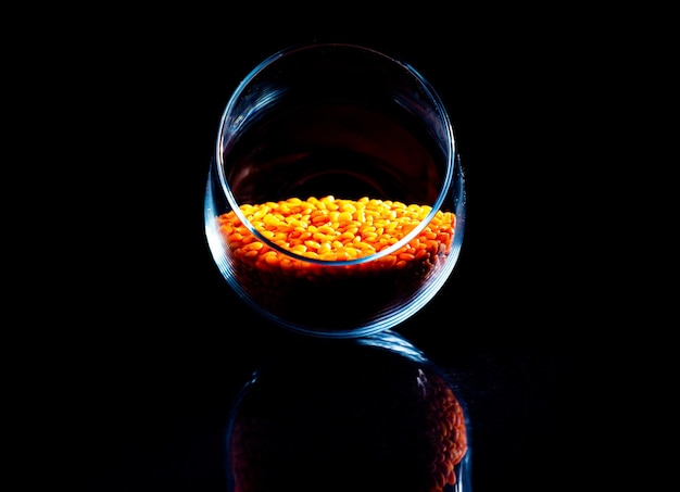 Close up of Raw Masur dal or masoor lentils or pink lentils in a black colored clay bowl on black in wineglass glass jar bucket