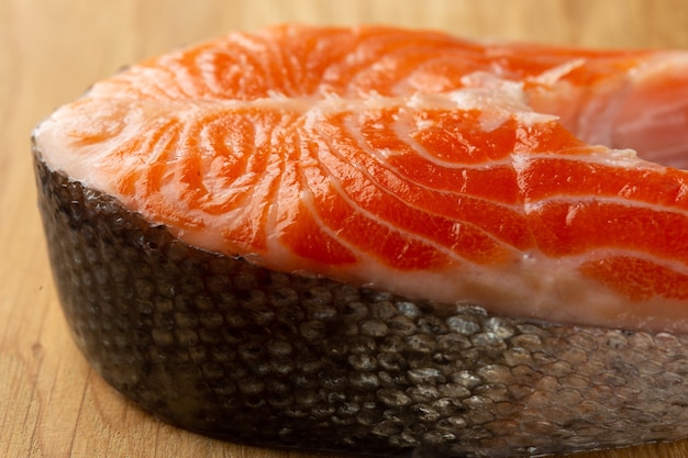 Close up of the raw red fish piece with shiny clean scale lying on the wooden table surface