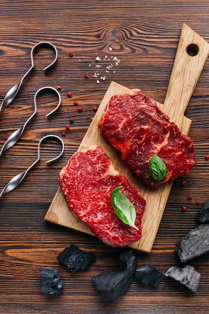 Photo close-up of raw steak with coal and metallic skewer on wooden backdrop