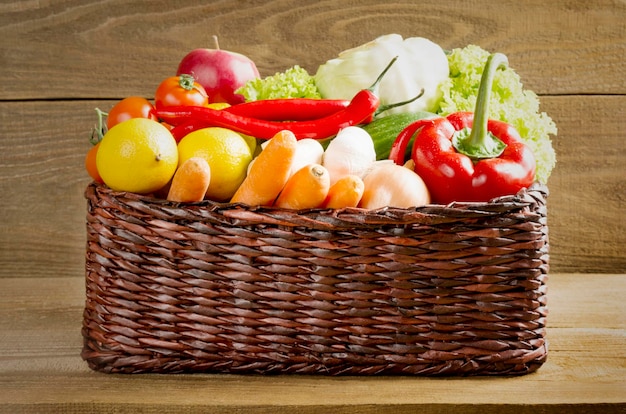 Close up of raw vegetables and fruits in wicker basket on wooden background