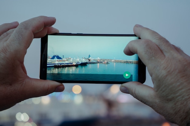 夕暮れの港で携帯電話で写真を撮るいくつかの手の背面図のクローズアップ