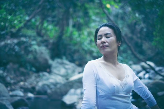森の中で蓮のヨガの位置で瞑想する女性のリアビューを閉じます