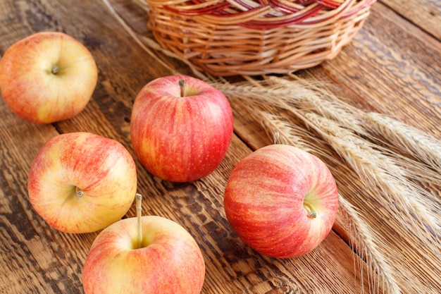 Крупным планом красные яблоки и колосья пшеницы на деревянных фоне. Малая глубина резкости.