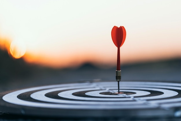 Photo close-up of red arrow hit center dartboard against sky during sunset