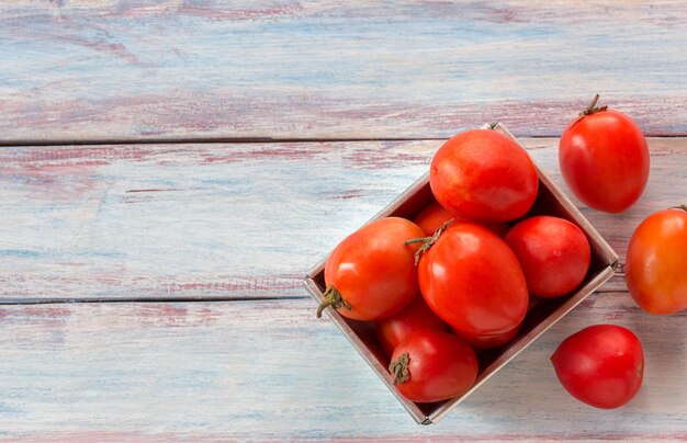 Close up red cherry plum tomatoes in stainless bowl on wood table background