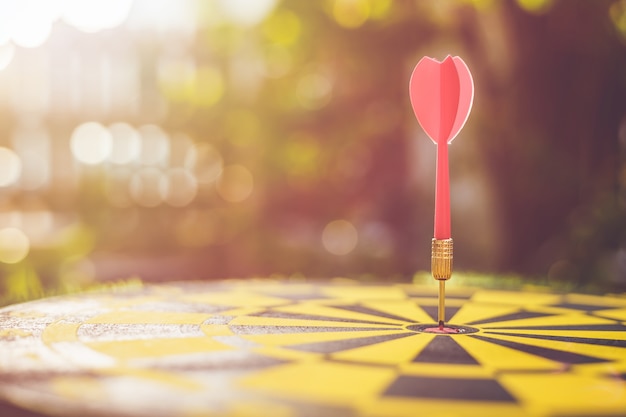 Close up red dart arrow in the center of dartboard. Blur and bokeh in sunrise time 