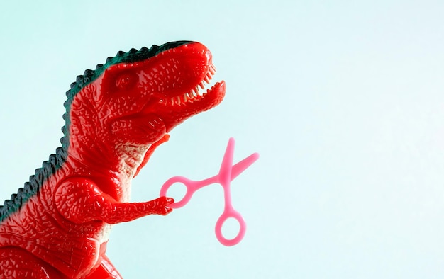 Close up red dinosaur holding tiny scissors Beauty care hairdressing concept