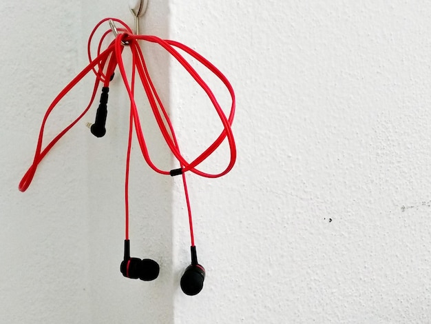 Photo close-up of red in-ear headphones hanging against white wall