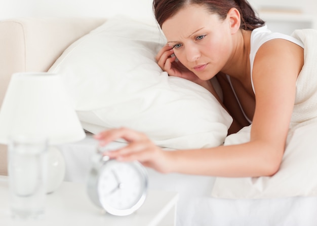 Close up of a Red-haired woman lying in bed turning off alarm cl