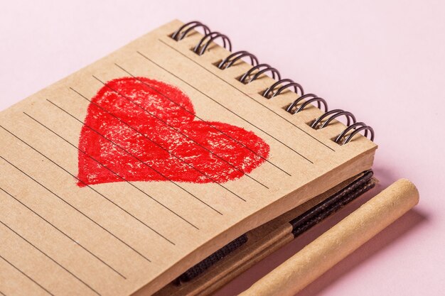 Close-up of a red heart painted in a recycled paper notebook and a pen