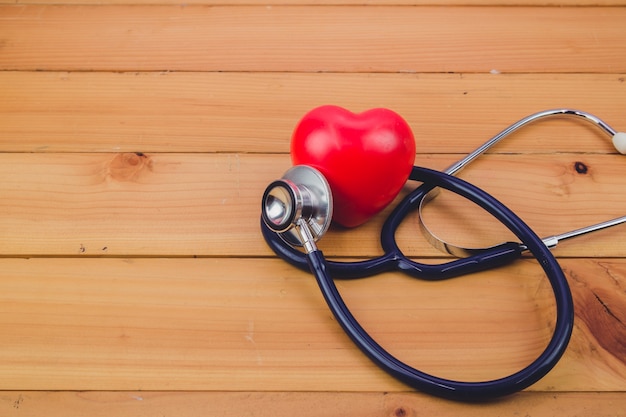 Close up red heart and steythoscope on old wood table