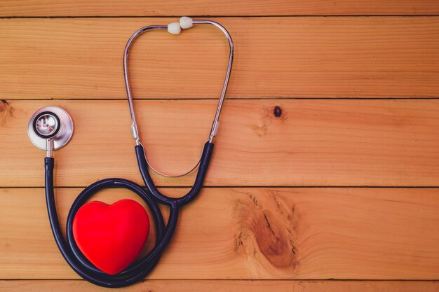 Close up red heart and steythoscope on old wood table