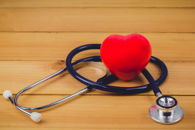 Close up red heart and steythoscope on old wood table